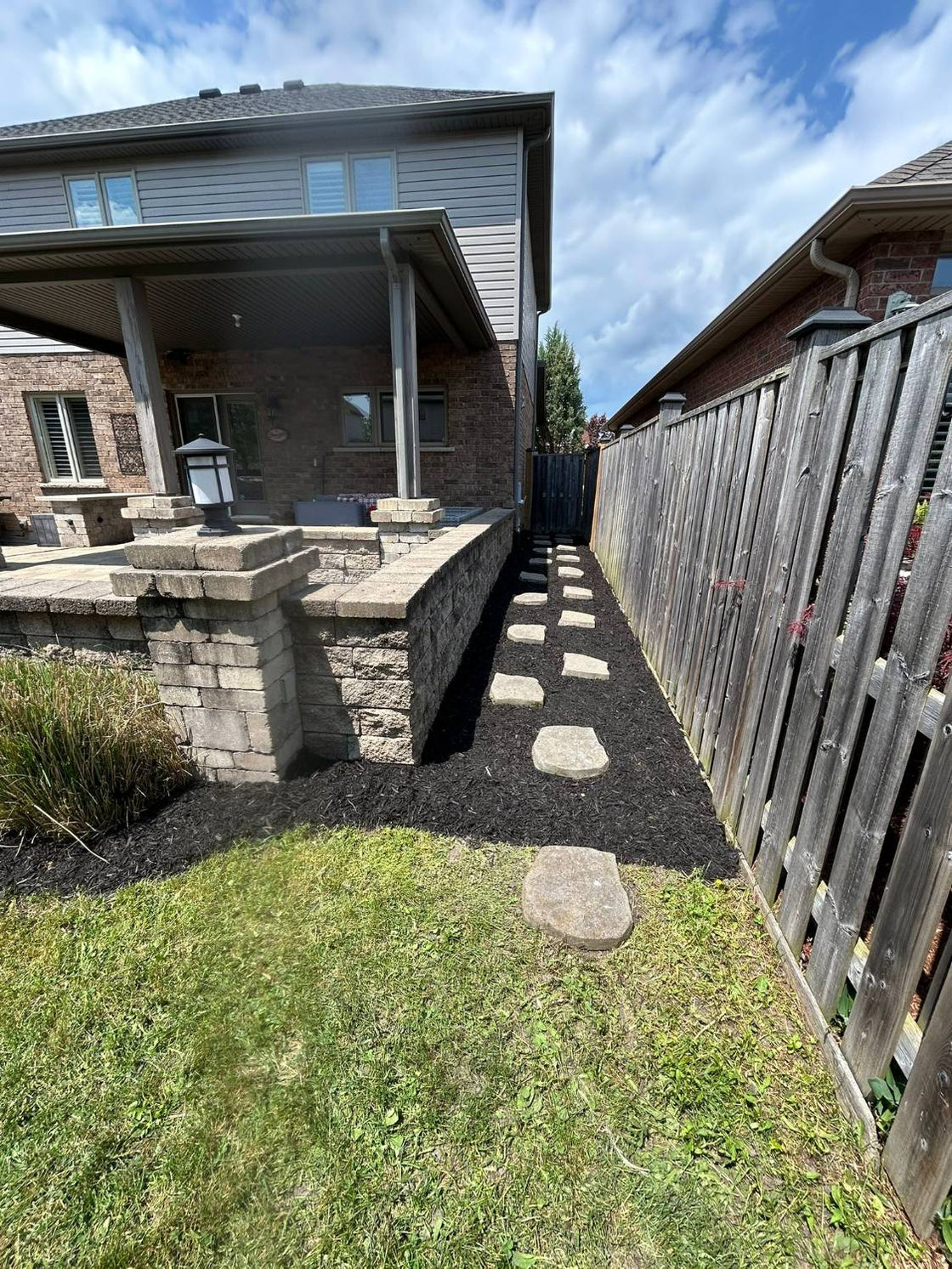 Fresh black mulch bed down a side yard, with stepping stones, a cleanly cut lawn edge and a wood fence